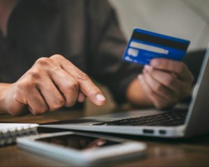 an unseen person holds a credit card while typing on a laptop