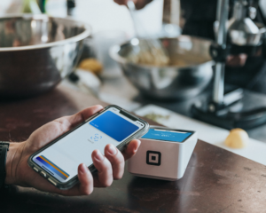 a hand holds a smartphone near a pay terminal for a tap-to-pay transaction