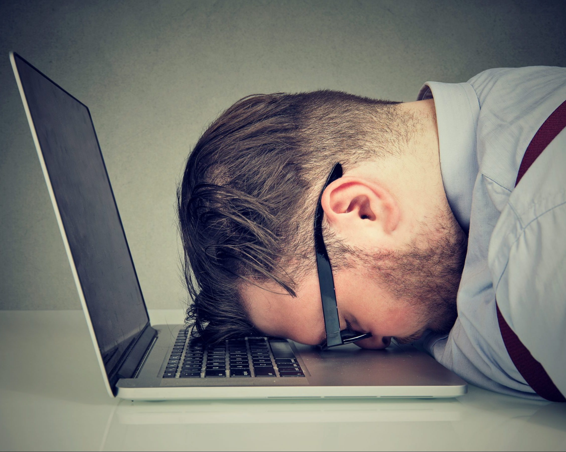 Side view of man looking broken while lying on top of laptop.