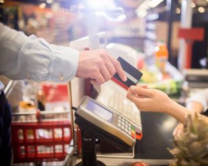 an unseen person gives their credit card to a cashier at a supermarket
