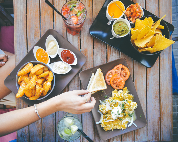 A woman's hand reaches across a table with three appetizer plates to grab some food.