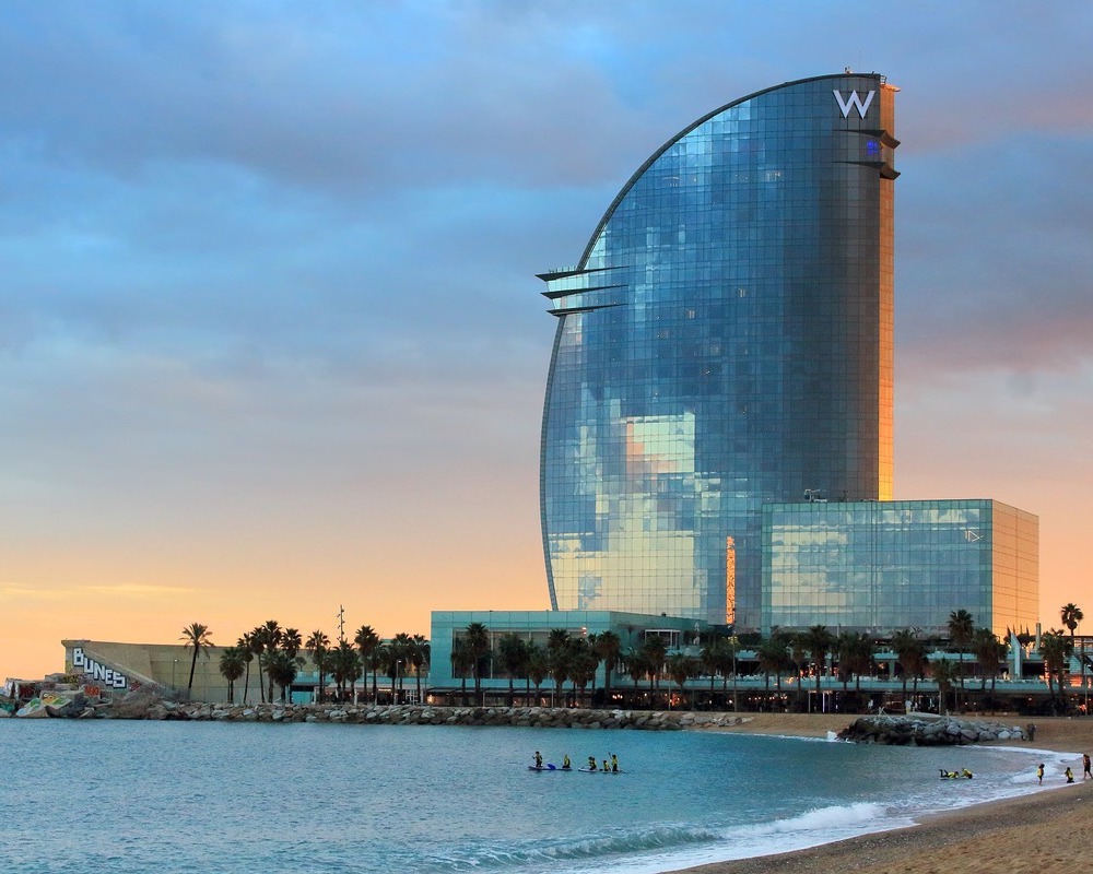 a glass-fronted hotel with curved designs sits near a beach; you can book hotels like this one using Marriott points earned from hotel credit cards with no annual fee