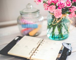 Photo of a calendar planner book open with a flower vase and a vase of chalk in the background