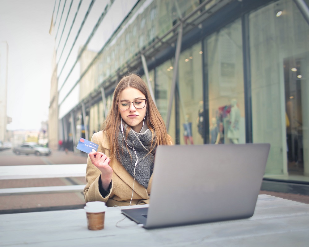 a woman sits at a laptop while holding a credit card