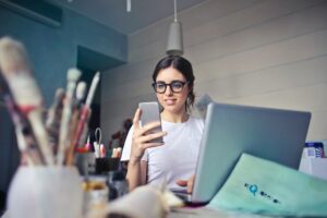 Small business woman looking at phone with art supplies around