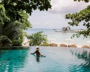 a woman in an infinity pool overlooking a beach and ocean