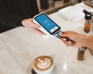 an unseen person inserts a credit card into a card reader to pay for a latte at a coffee shop