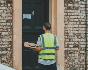 A man with a yellow safety vest waits at a door to deliver an Amazon package