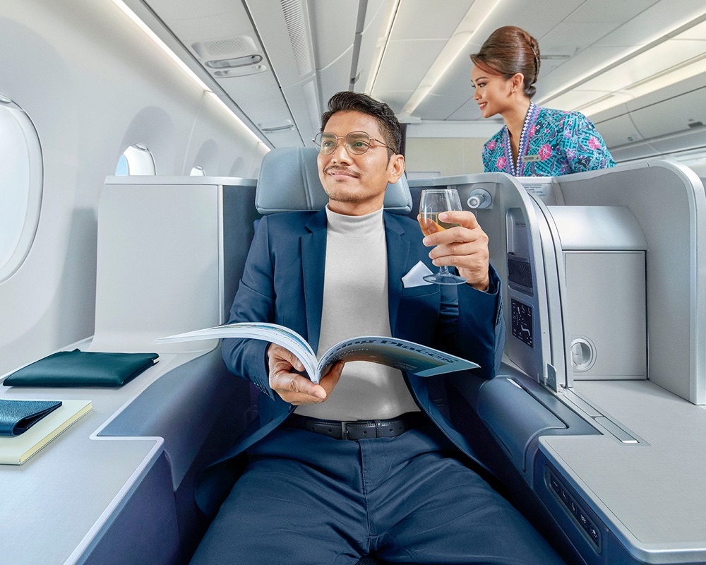 a passenger reads a magazine and has a drink in Malaysia Airlines business class