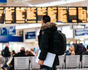 a traveler holding a laptop looks at flight departure screens at an airport