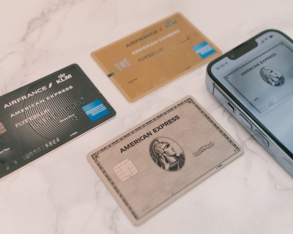 Three American Express credit cards arranged next to a phone displaying a virtual card on a desk