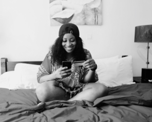 a woman sits on her bed looking at her phone while holding a credit card