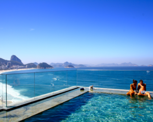 a couple in a hotel pool with the beaches of Rio de Janeiro and Sugerloaf Mountain visible beyond