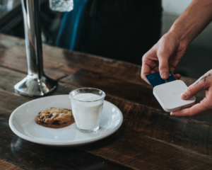 a plate of cookies and glass of milk sit on a counter while someone swipes a credit card