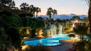 a picture at dusk of a pool with waterfalls into it and palm trees in the background