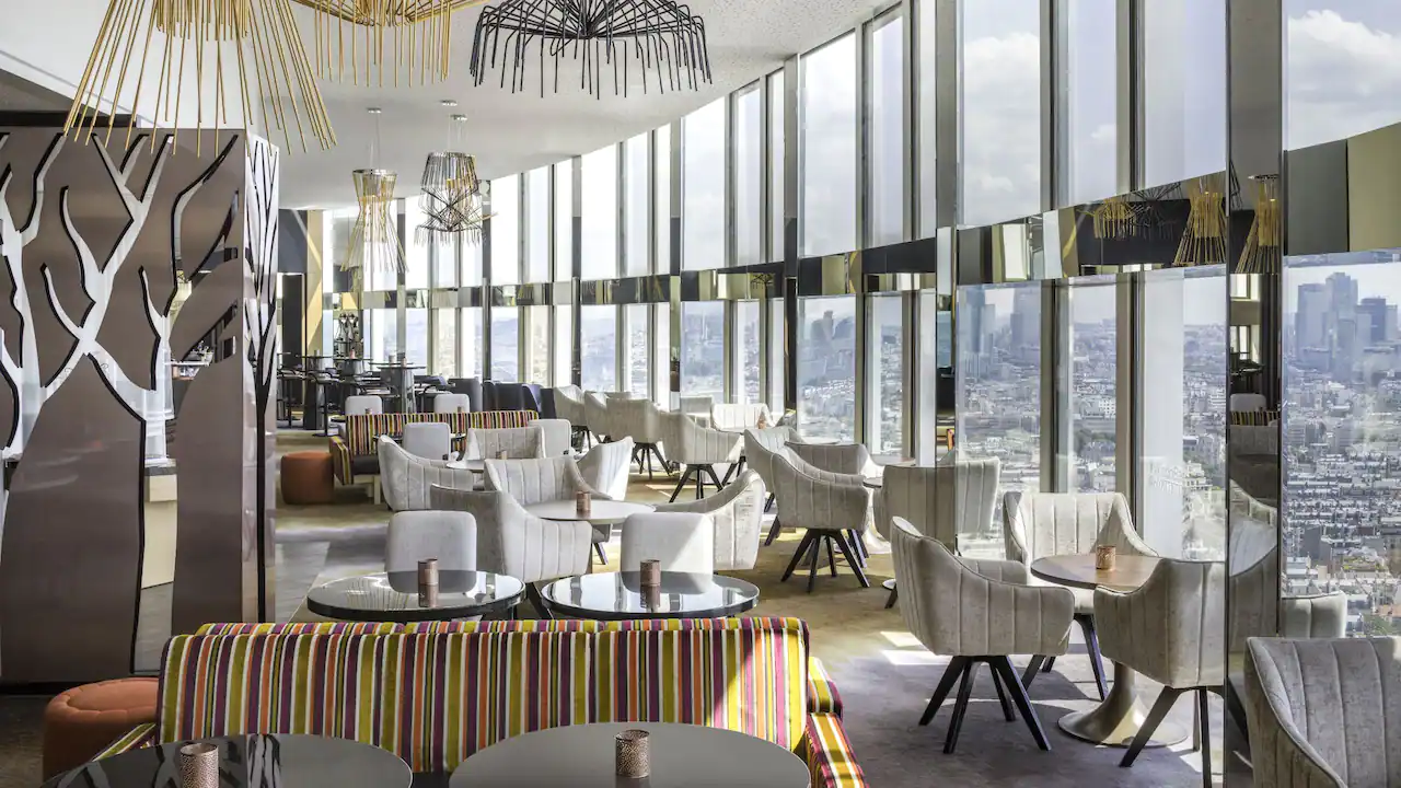restaurant tables and white chairs with floor-to-ceiling glass windows overlooking paris