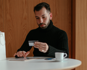a man sits at a table, holding a credit card and using a tablet