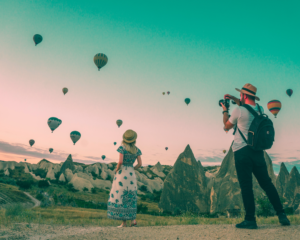 a couple takes pictures together in front of hot air balloons in Cappadocia