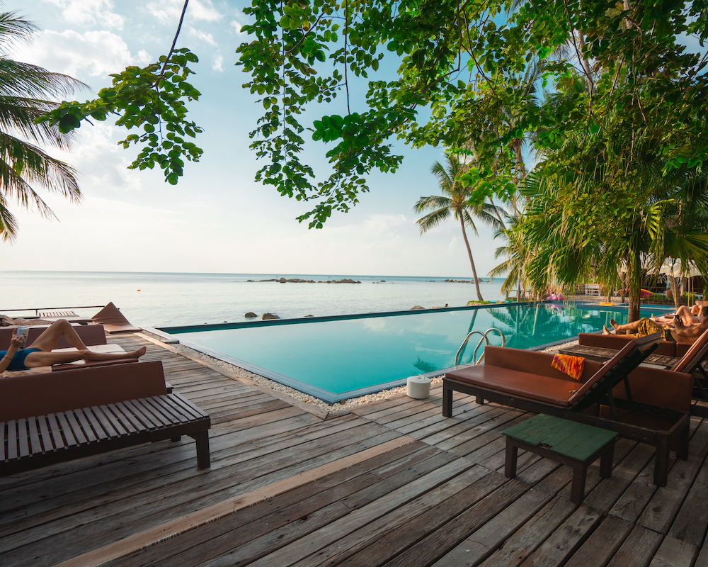 people lay around a hotel pool near a beach