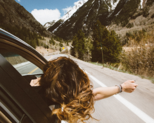 a passenger leans out the window of a car as it winds through a mountain road