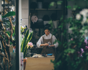 looking between plants to see a shop owner inside a floral shop