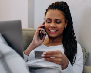 a woman talks on the phone while looking at her credit card and a laptop
