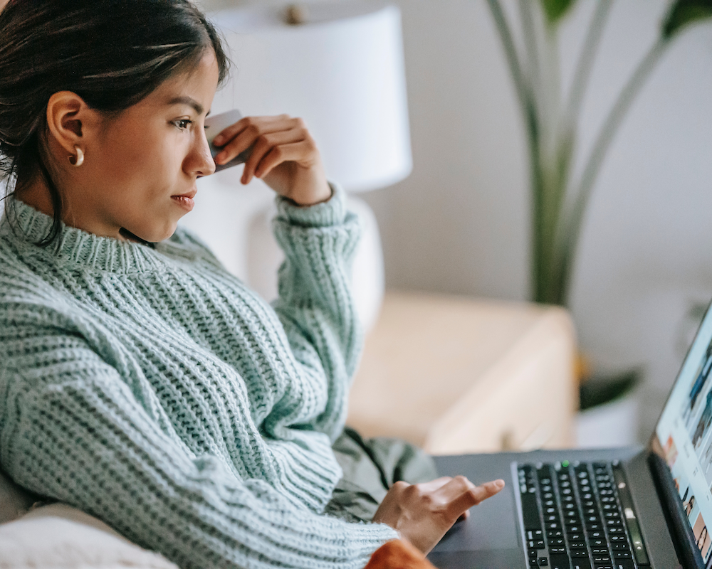 a woman lays on a bed while looking at her laptop