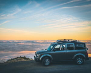 an SUV parked on a hilltop overlooking clouds at sunrise