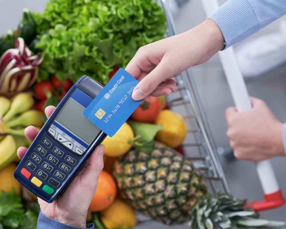 overhead view of a hand tapping a credit card on a payment machine when paying for groceries