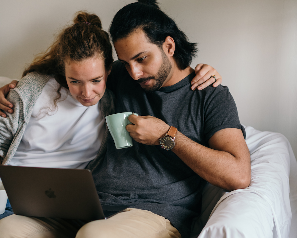 a couple looks at a laptop together while sitting on a sofa