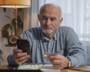 A man sits at a table holding a credit card while looking at his smart phone