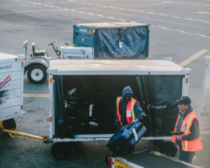 baggage handlers load luggage onto carts, as seen from a plane window