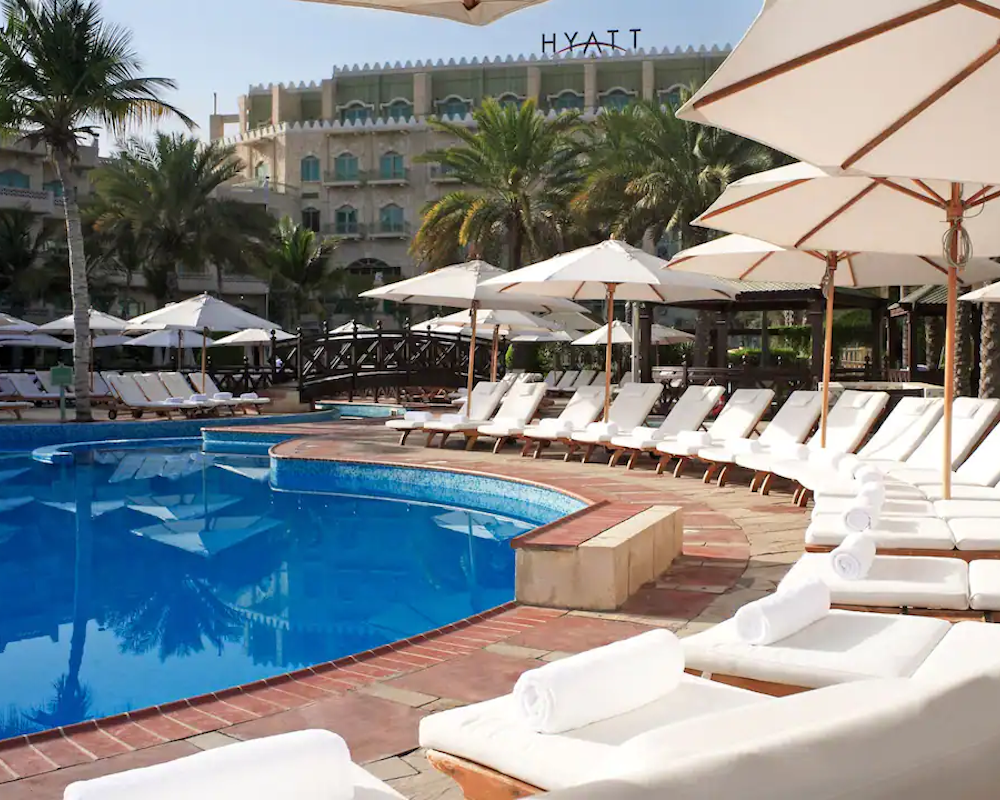 lounge chairs around a pool with the Hyatt logo on the hotel tower