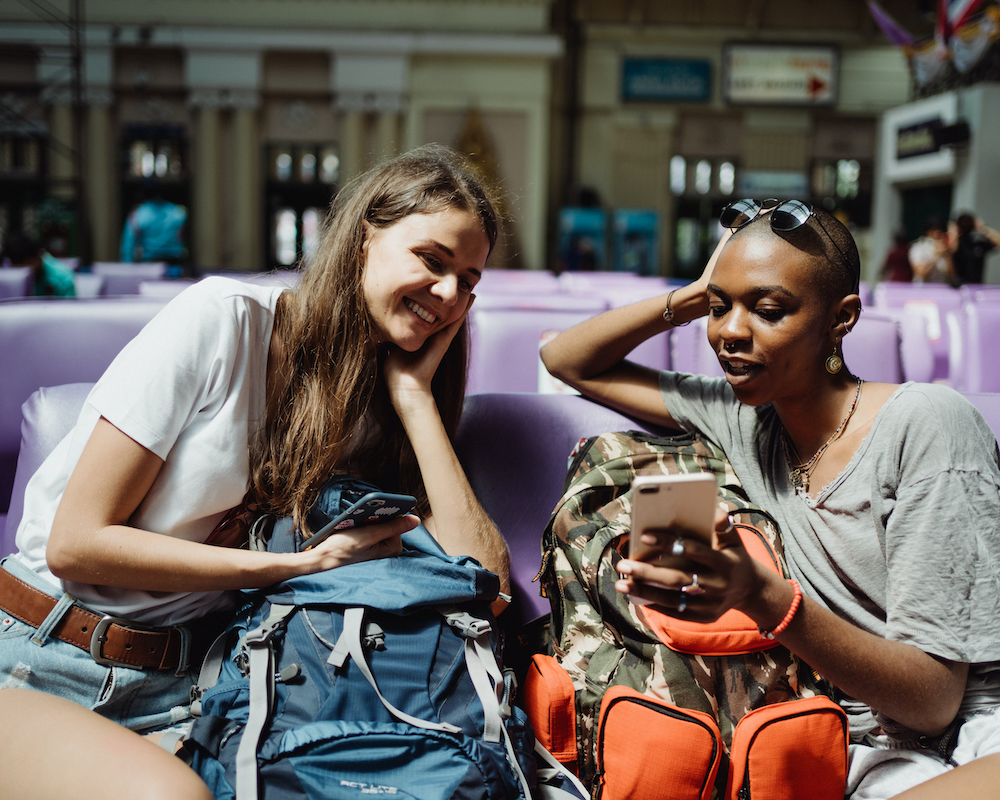 friends look at a phone together while waiting in an airport