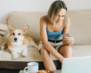 A woman holds a credit card and laptop while sitting next to a dog