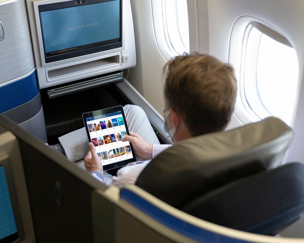 a passenger in United Polaris business class using an iPad and view of the inflight entertainment system