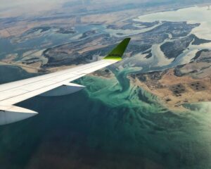 an airBaltic wing tip visible from a plane window while flying over water