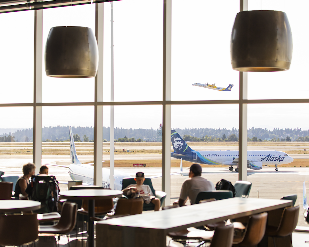 an Alaska Airlines plane is visible through the windows of an airport lounge