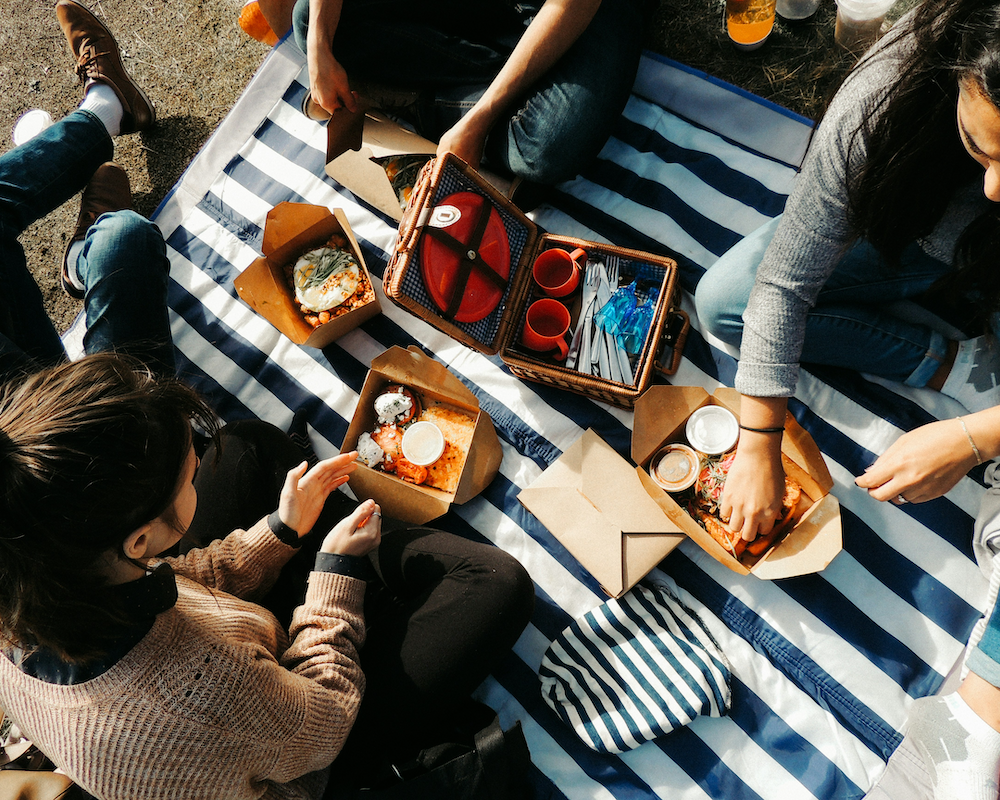 overhead view of friends eating food from takeout boxes during a picnic in the park