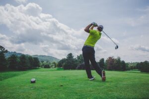 man in hat swinging a golf club, shown from behind