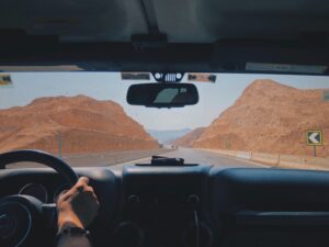 view of a person from behind the wheel driving toward desert mountains