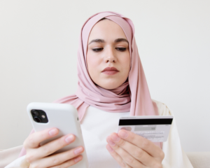 a woman in a hijab holds a cell phone and credit card