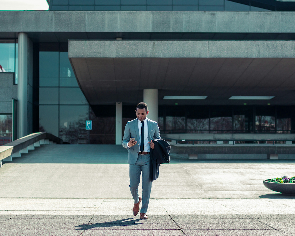 a man in a suit checks his phone while walking out of a building