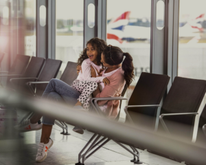 A daughter sits on her mom's lap with British Airways planes visible outside the window