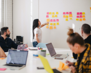 a business meeting where one person is pointing to stick notes on the wall