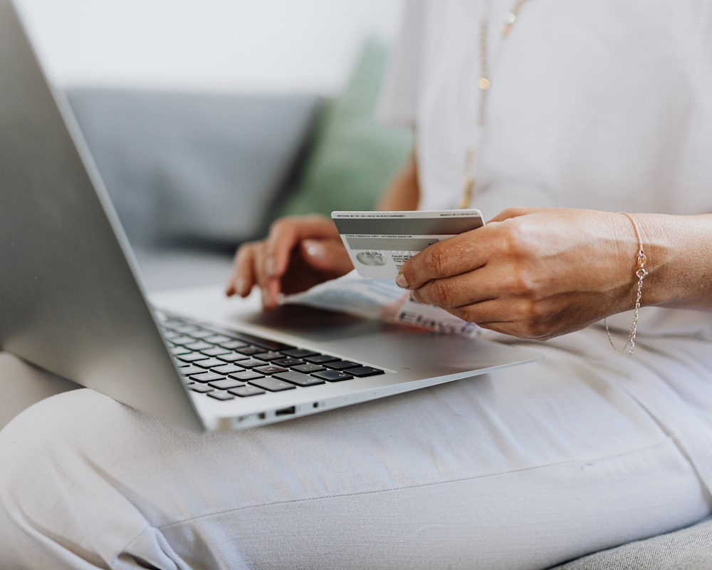 a close-up of a laptop sitting on someone's lap while a hand holds a credit card
