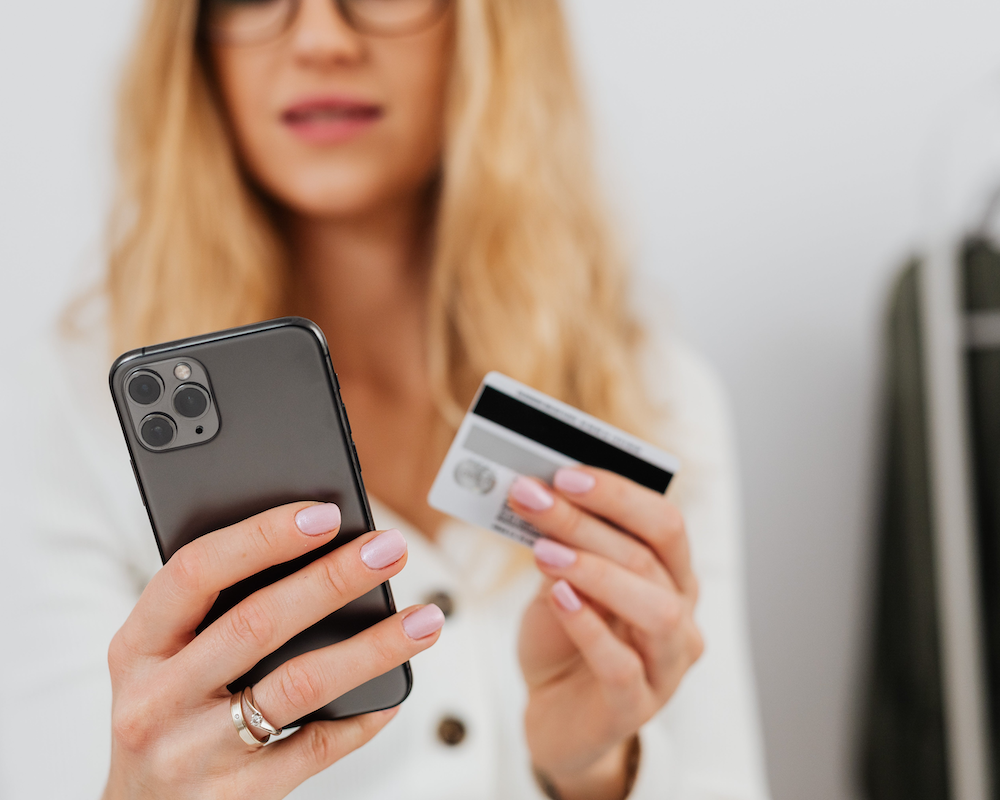a woman holds a credit card while reading information about it on her smart phone