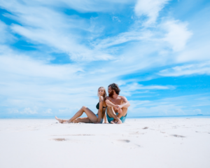 a couple sits together in the sand on a sunny day