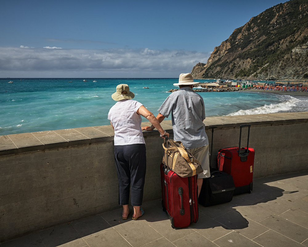 a couple with suitcases pauses at the edge of a walkway to look over the ocean