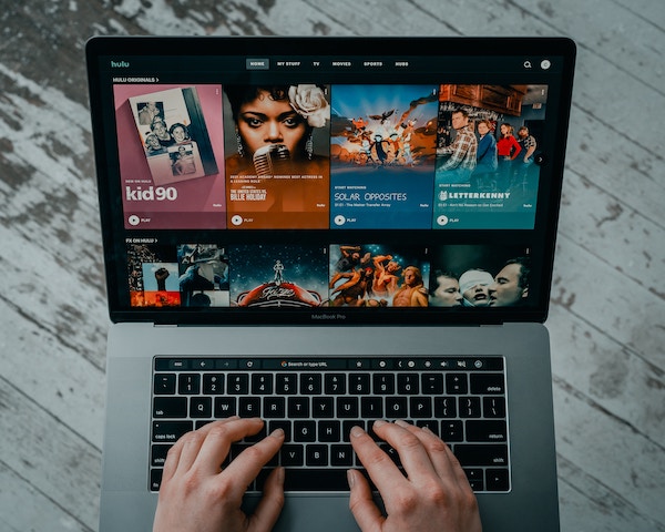 Two hands rest on a laptop keyboard with the Hulu homepage on the screen. The right credit card can give you rewards or cash back for streaming services.